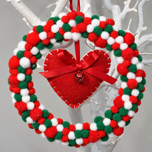 A red, white, and green pom-pom wreath with a red felt heart in the center.