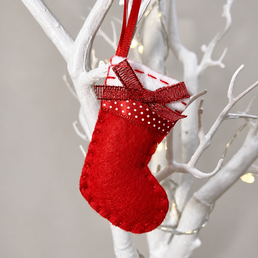 Red felt Christmas stocking ornament with a polka dot bow hanging on a white branch.