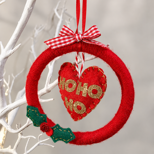 Red Christmas wreath with a heart-shaped ornament that says "HO HO HO" in gold glitter.
