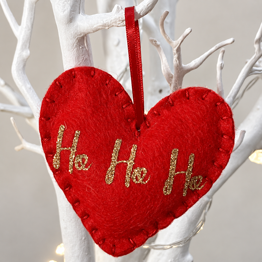 Red felt heart ornament with "Ho Ho Ho" in gold glitter, hanging from a white branch.
