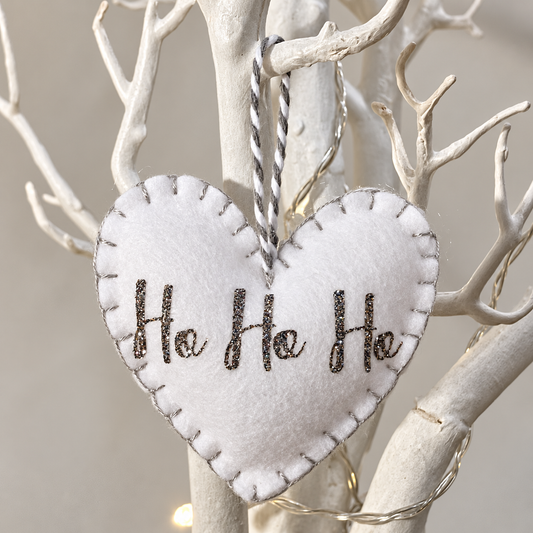 White felt heart ornament with "Ho Ho Ho" in glitter, hanging from a white branch.