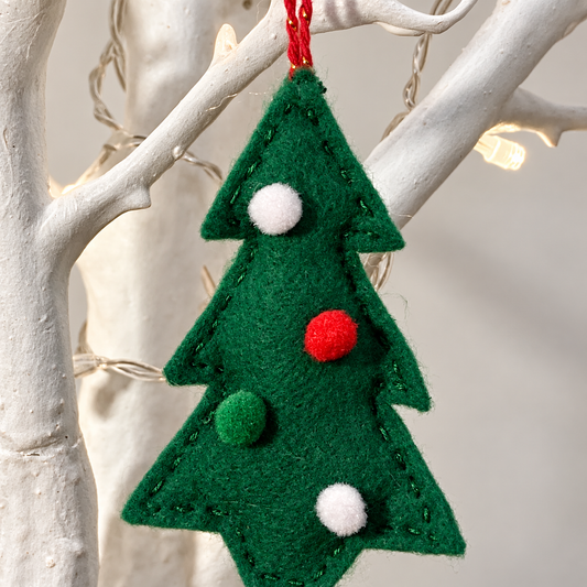 Handmade green felt Christmas tree ornament with red and white pom-poms, hanging on a white branch.
