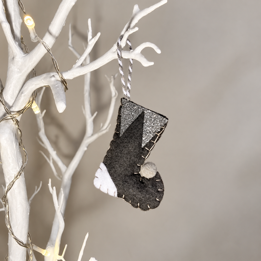 Handmade black felt Christmas stocking with white and silver accents hanging on a white branch.