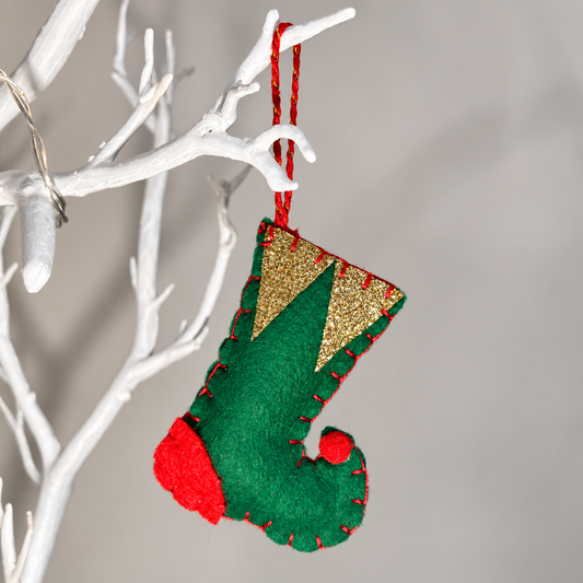 Green felt Christmas stocking with gold glitter cuff and red accents, hanging on a white branch.