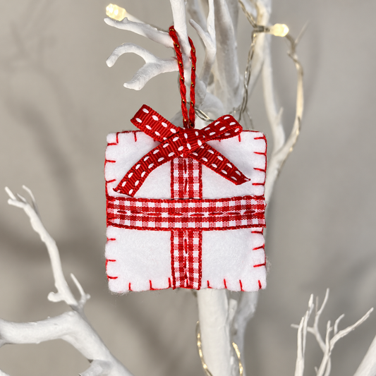 White felt gift ornament with red and white plaid ribbon, hanging from a white branch.