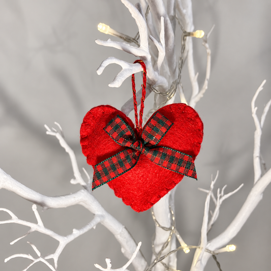 Red felt heart ornament with a plaid bow hanging from a white branch.