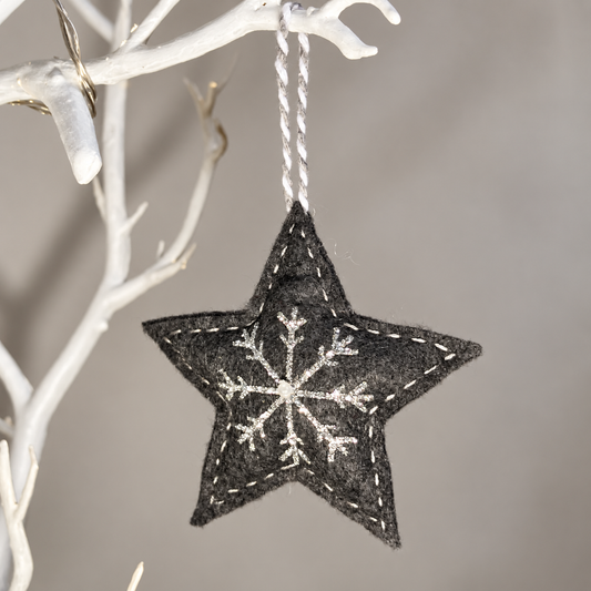 Dark gray felt star ornament with white snowflake embroidery hanging from a white branch.