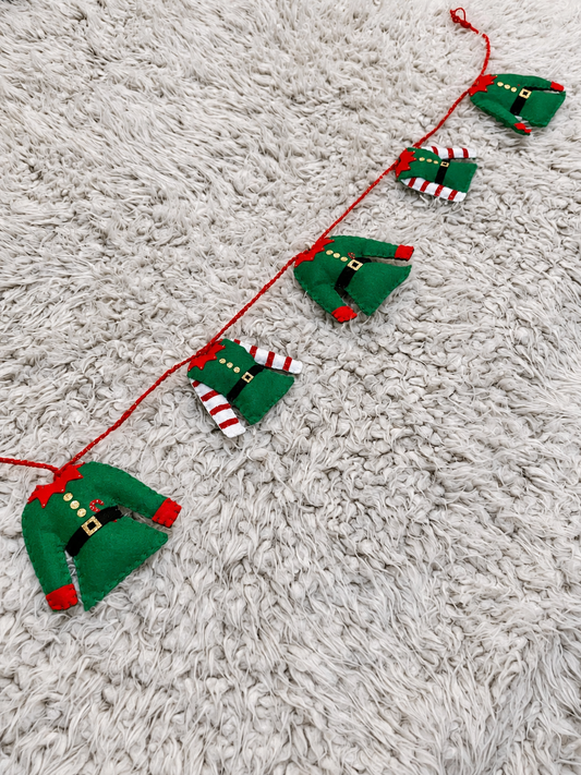 Christmas garland with five elf outfits hanging on a red string.