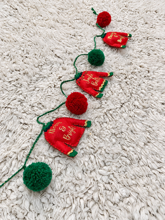 Christmas garland with red sweaters and green and red pom-poms on a white shag rug.