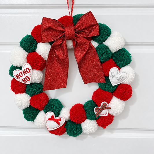 Christmas wreath made of red, green, and white pom-poms with a large red glitter bow.