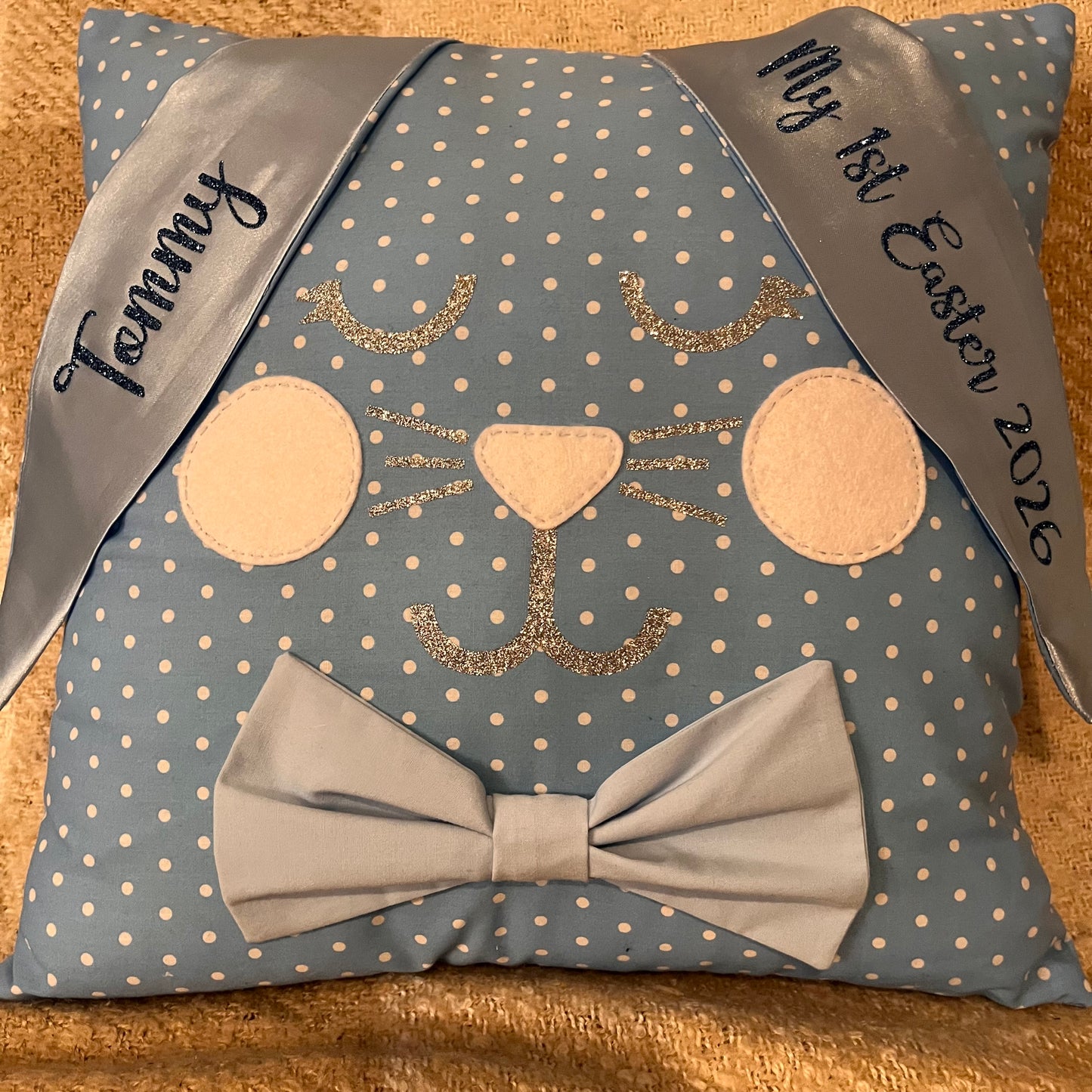 Blue polka dot pillow shaped like a bunny with a bow tie and personalized ribbons.