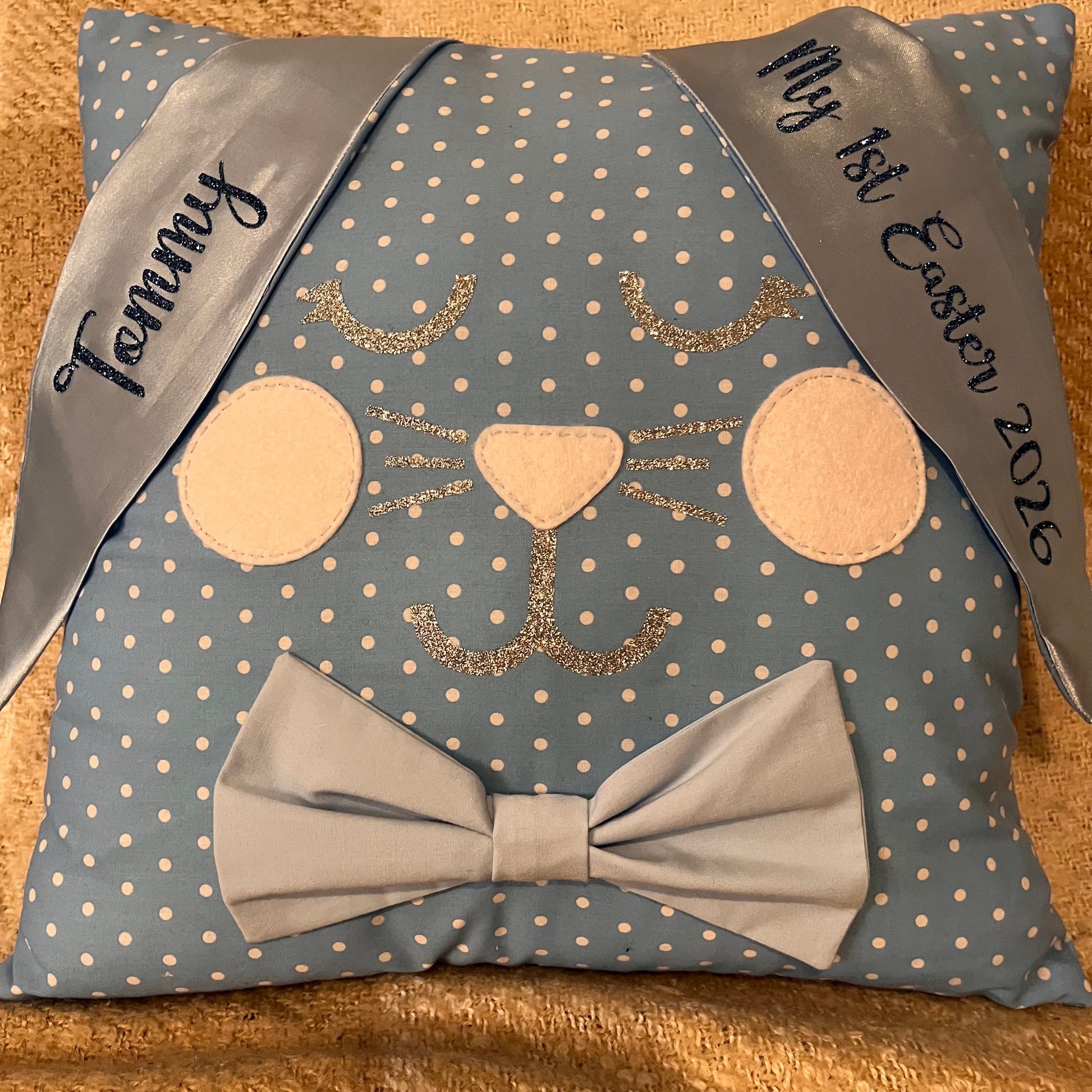 Blue polka dot pillow shaped like a bunny with a bow tie and personalized ribbons.