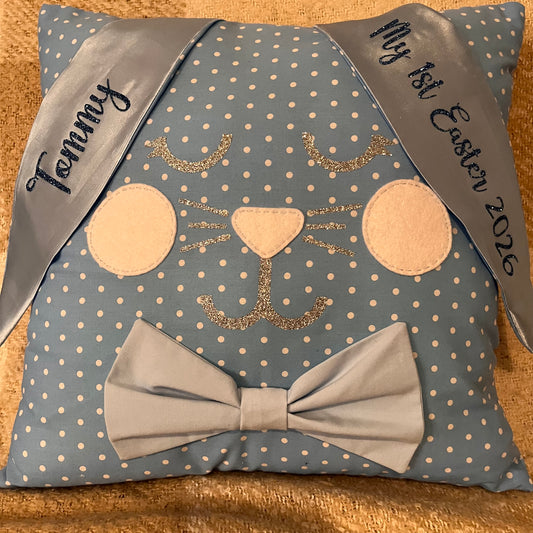 Blue polka dot pillow shaped like a bunny with a bow tie and personalized ribbons.
