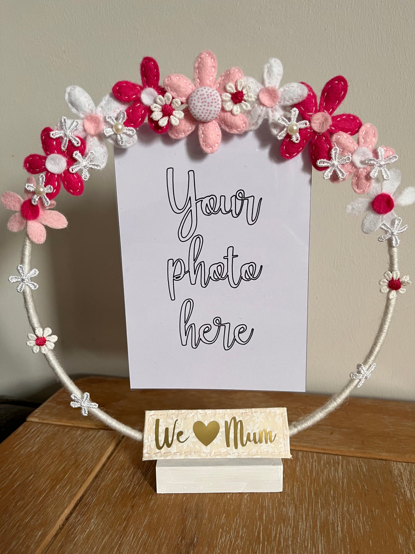 A white hoop photo frame decorated with pink, white, and red felt flowers, with a We Love Mum sign.