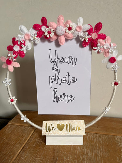 A white hoop photo frame decorated with pink, white, and red felt flowers, with a We Love Mum sign.