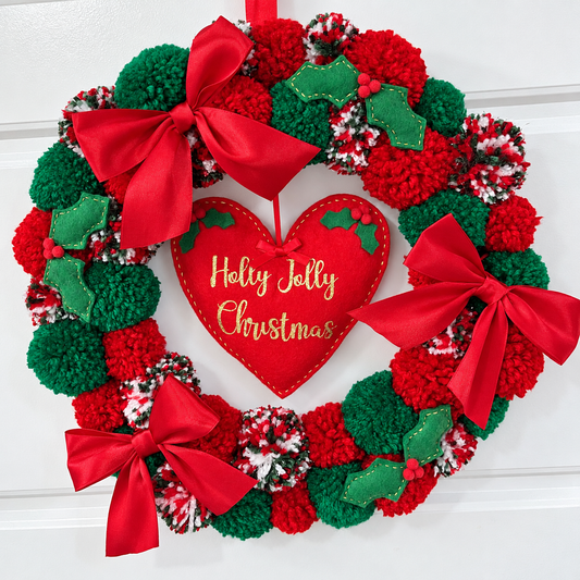 A festive Christmas wreath made of red and green pompoms with a heart in the center.