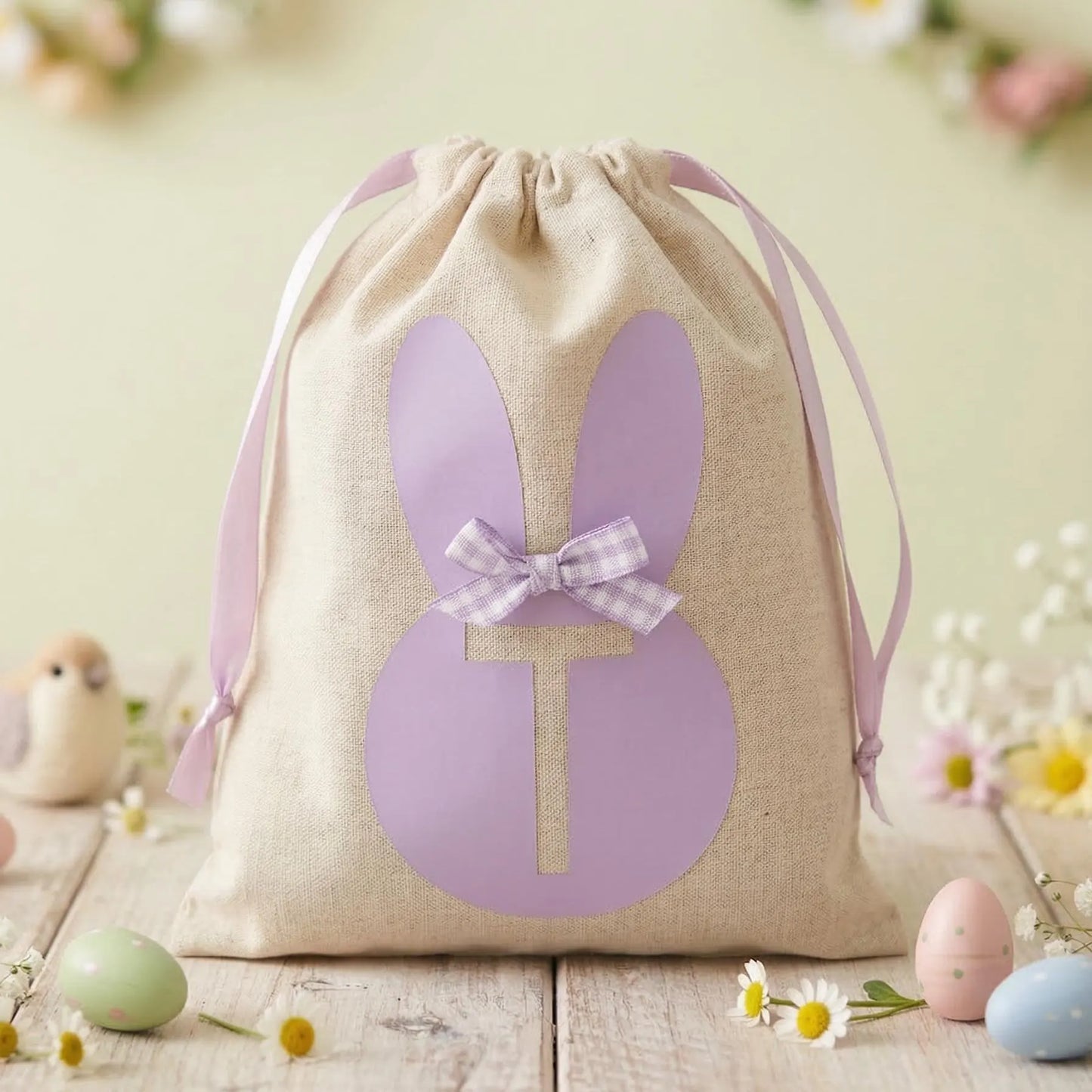 Linen drawstring bag with a purple bunny silhouette and initial T, surrounded by Easter eggs and daisies