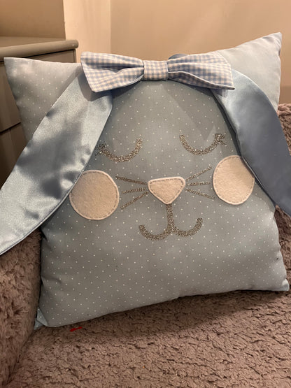 Light blue polka dot pillow with a bunny face, glittery whiskers, and a gingham bow.