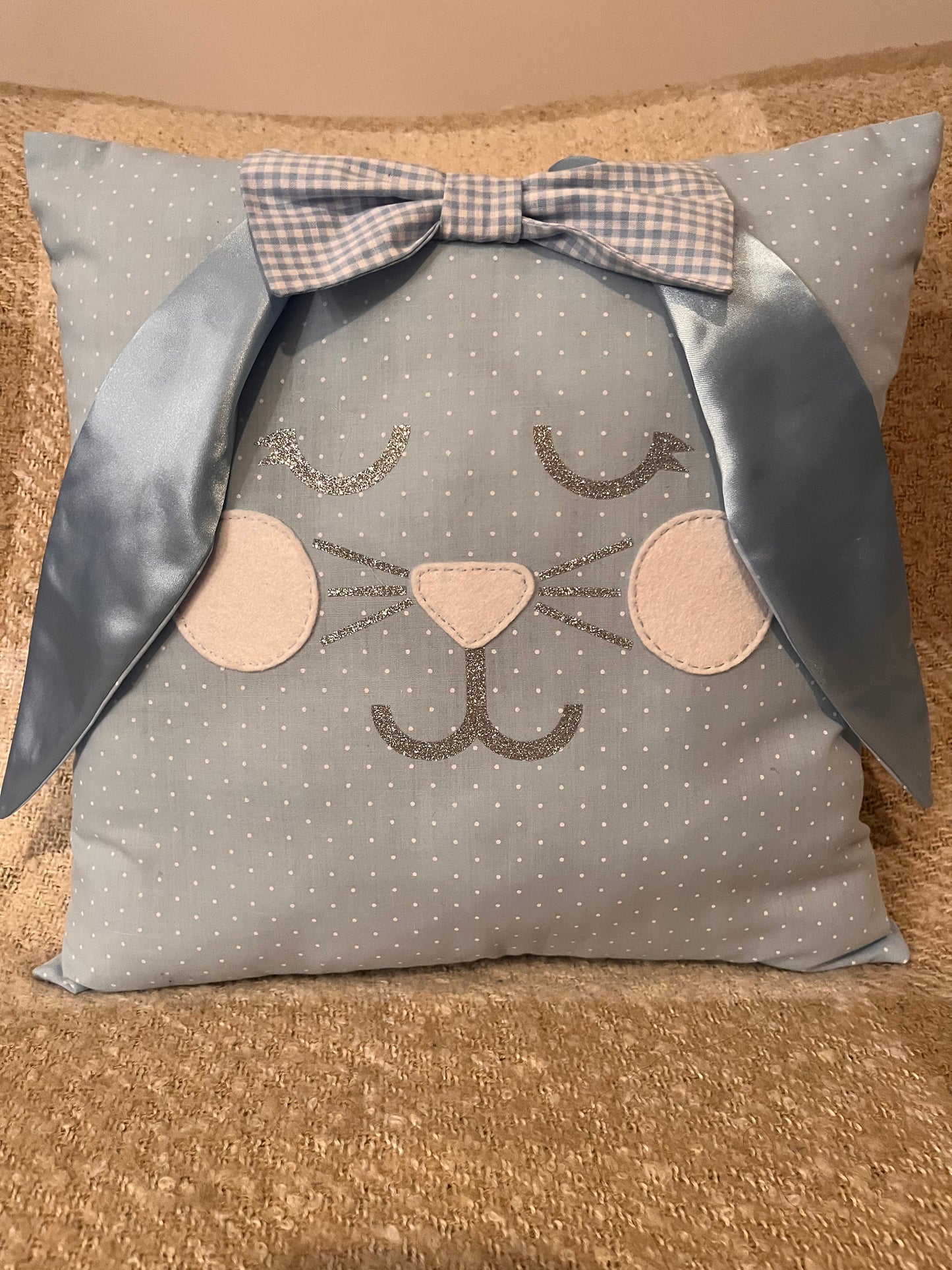 Light blue polka dot pillow with a bunny face, glittery eyelashes, nose, and whiskers, and blue satin ears.
