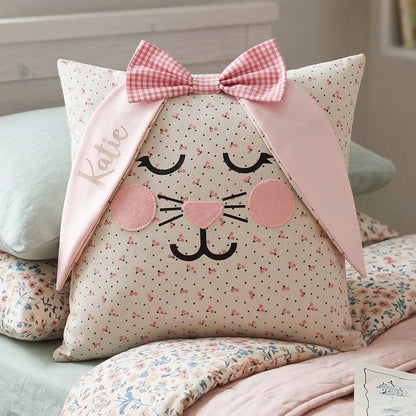 A bunny-shaped pillow with a pink gingham bow and the name Katie embroidered on one ear. It has a dotted pattern.