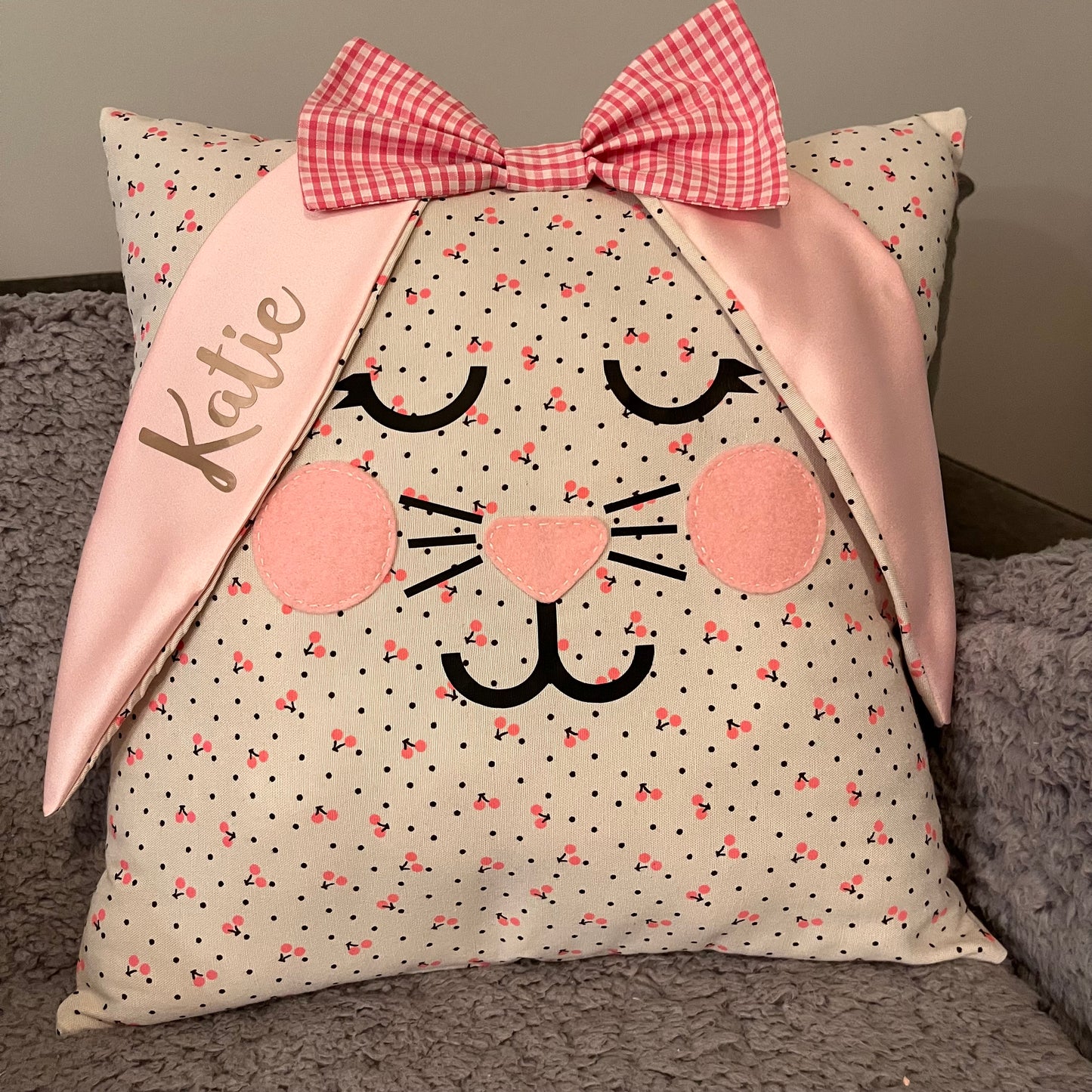 Bunny face pillow with pink gingham bow and ears, one ear personalized with Katie in gold script. 