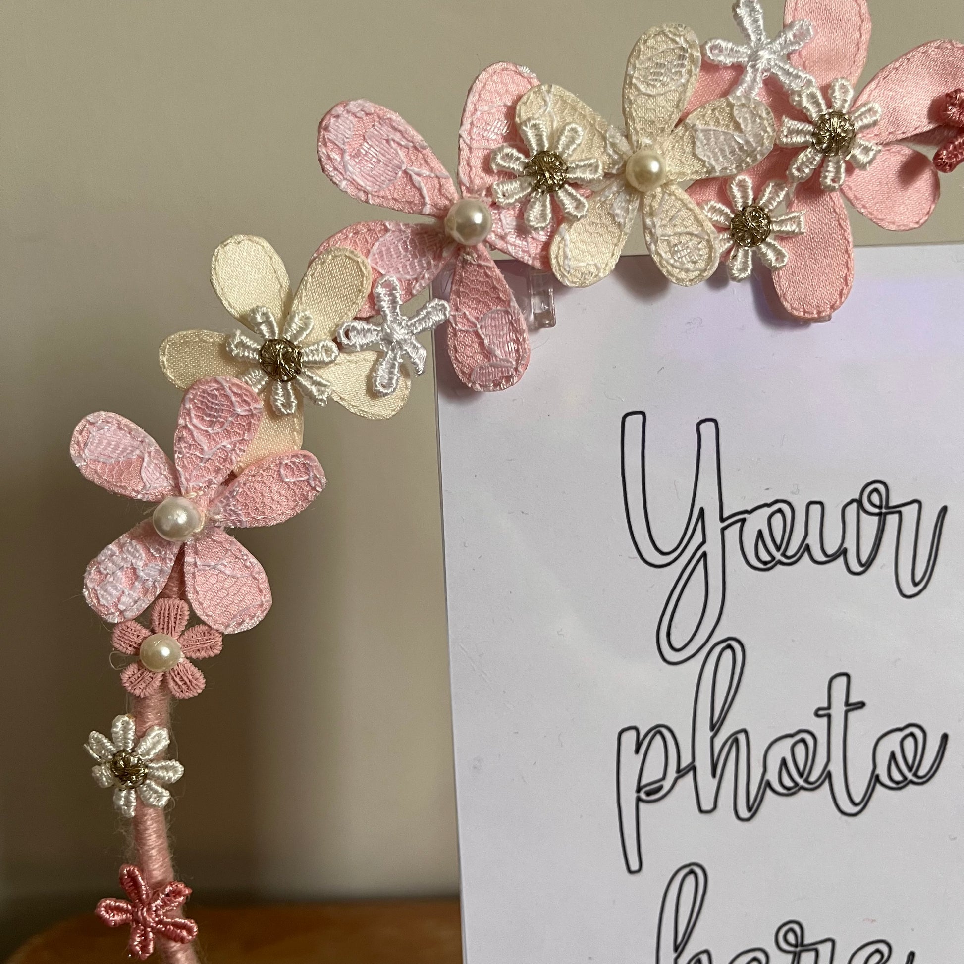 Close-up of a pink and cream floral headband with pearl and gold accents, next to a white card.